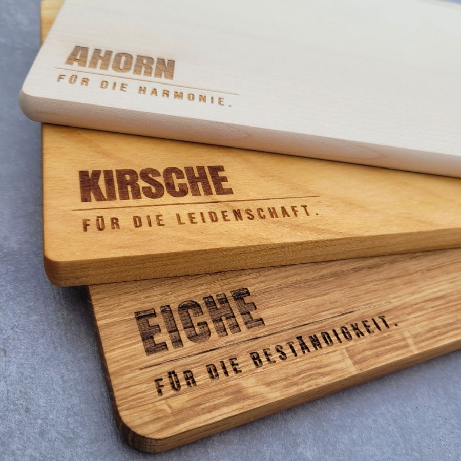Präzise Lasergravur auf Echtholz, Nahaufnahme der Schriftzüge Beständigkeit, Harmonie und Leidenschaft auf verschiedenen Holzarten.